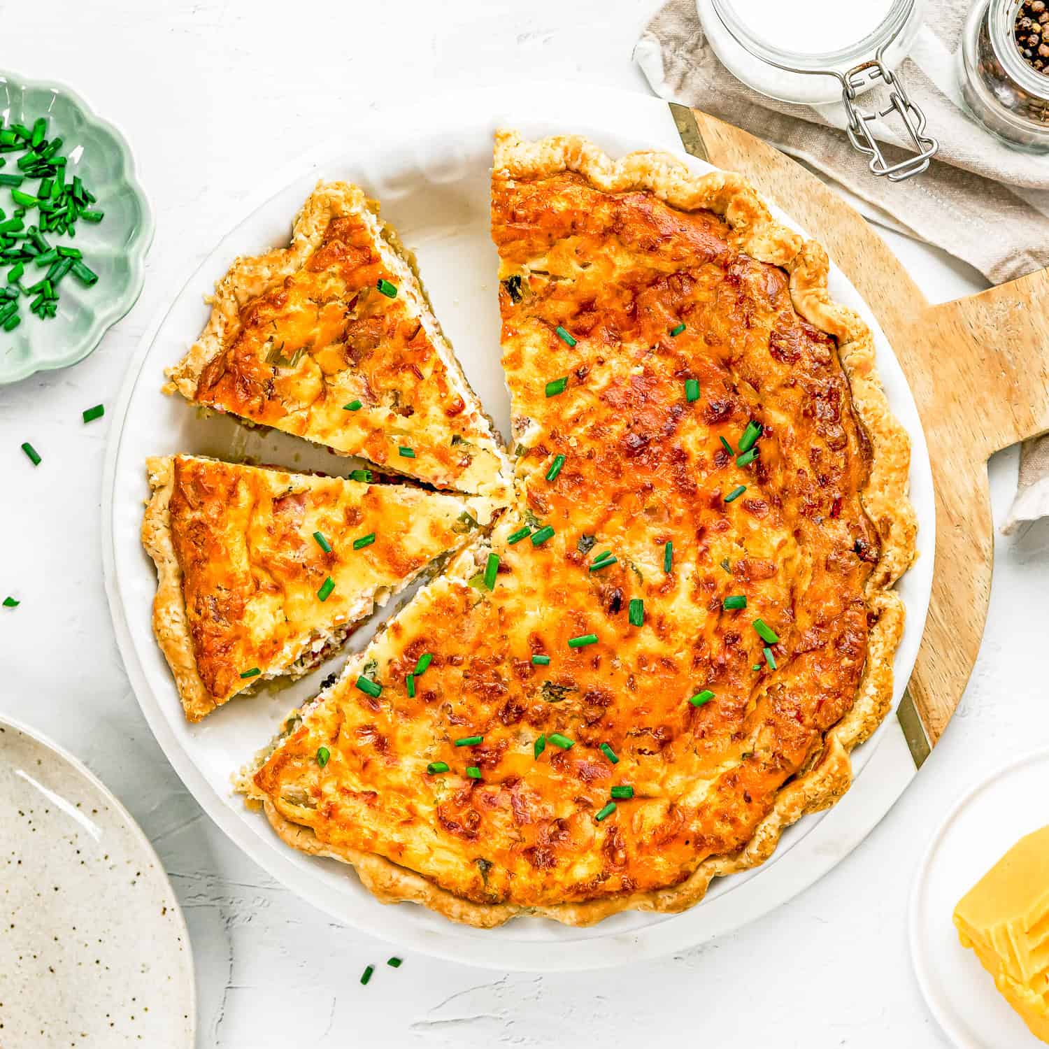 A baked quiche with a golden crust is cut into slices and garnished with chopped chives on a white plate, perfect for any egg-free breakfast recipes collection.