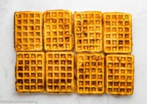 Eight rectangular Eggless Bacon Cheddar Savory Waffles are arranged in two rows on a white surface.