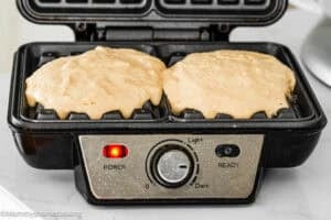 Eggless Banana Waffles batter poured in both slots of the waffle maker, power and ready indicator lights lit, with the control dial set to medium.
