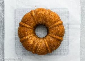 An Eggless Carrot Bundt Cake, golden brown and inviting, rests on a wire rack lined with parchment paper, viewed from above.