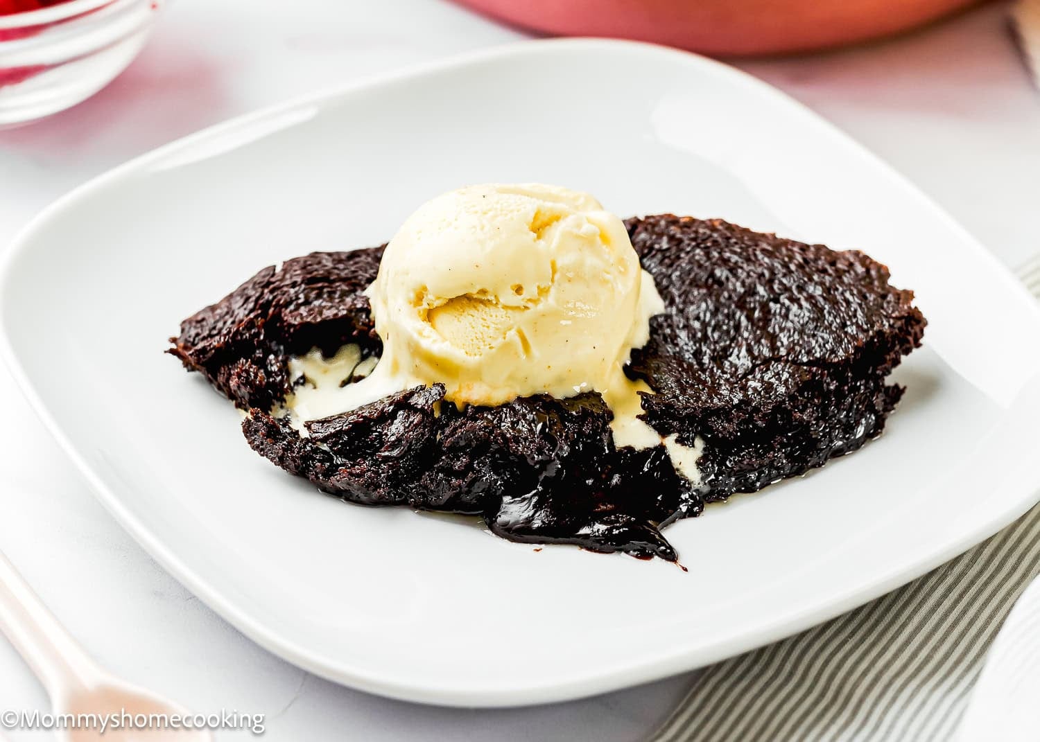 A serving of Eggless Chocolate Brownie Pudding (Ina Garten–Inspired) topped with a scoop of vanilla ice cream on a white plate.