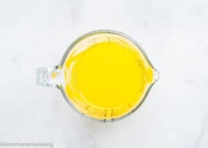 A glass measuring cup filled with melted yellow liquid, perfect for preparing Eggless Chocolate Brownie Pudding (Ina Garten–Inspired), sits on a white surface.