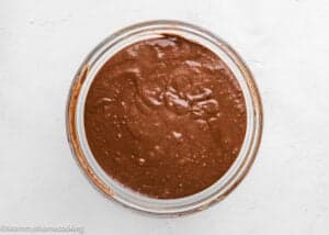 A glass bowl filled with eggless chocolate waffle batter sits on a white surface.