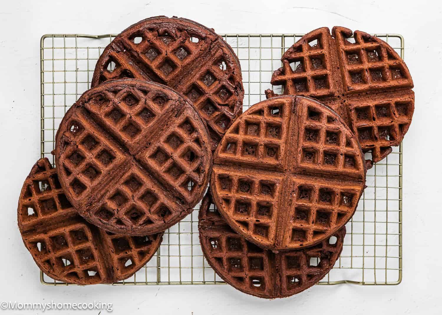 Six round Eggless Chocolate Waffles sit on a cooling rack atop a white surface.