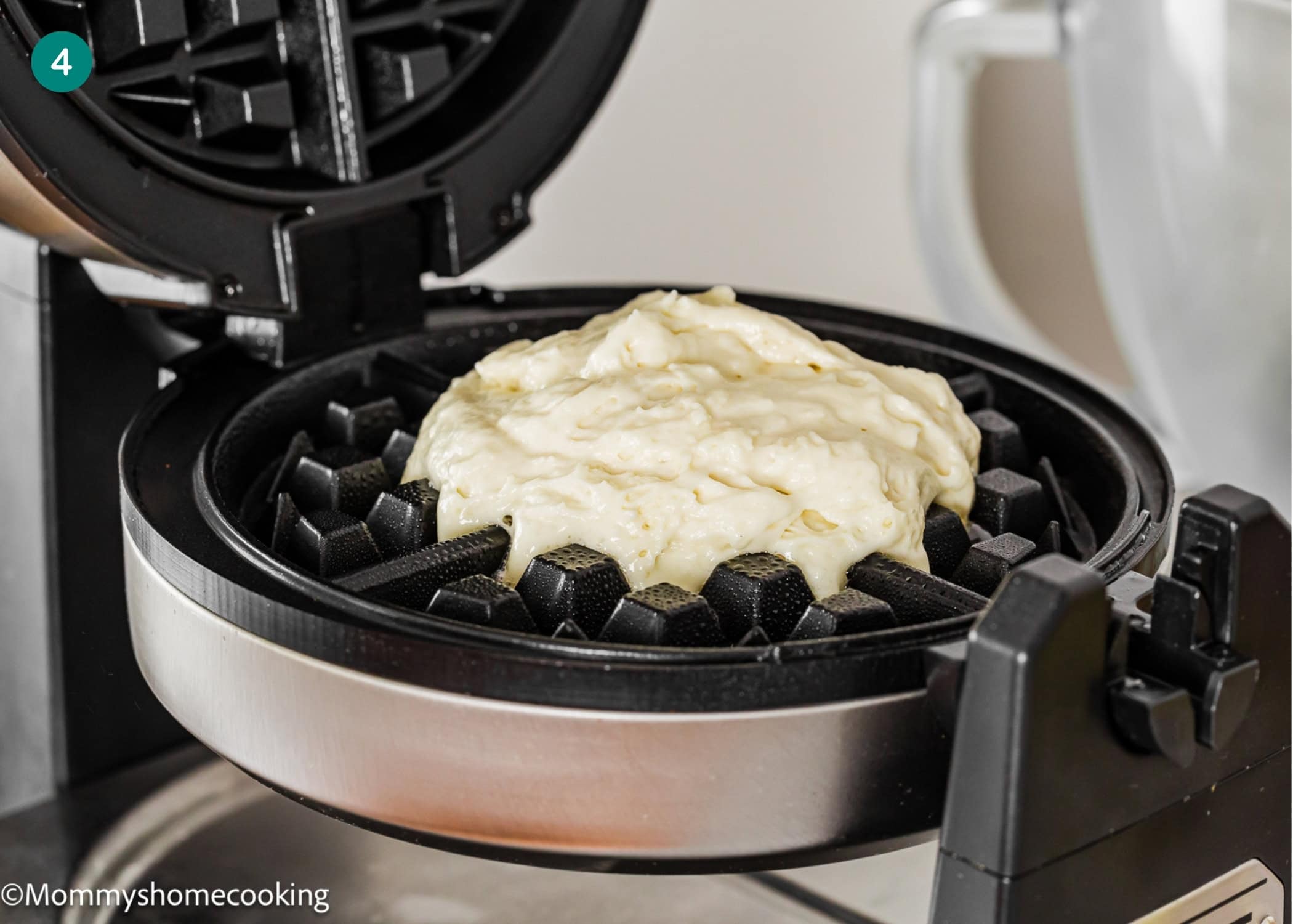 Waffle iron with raw Eggless Yogurt Waffles batter spread on the grates, ready to be cooked into a delicious waffle.