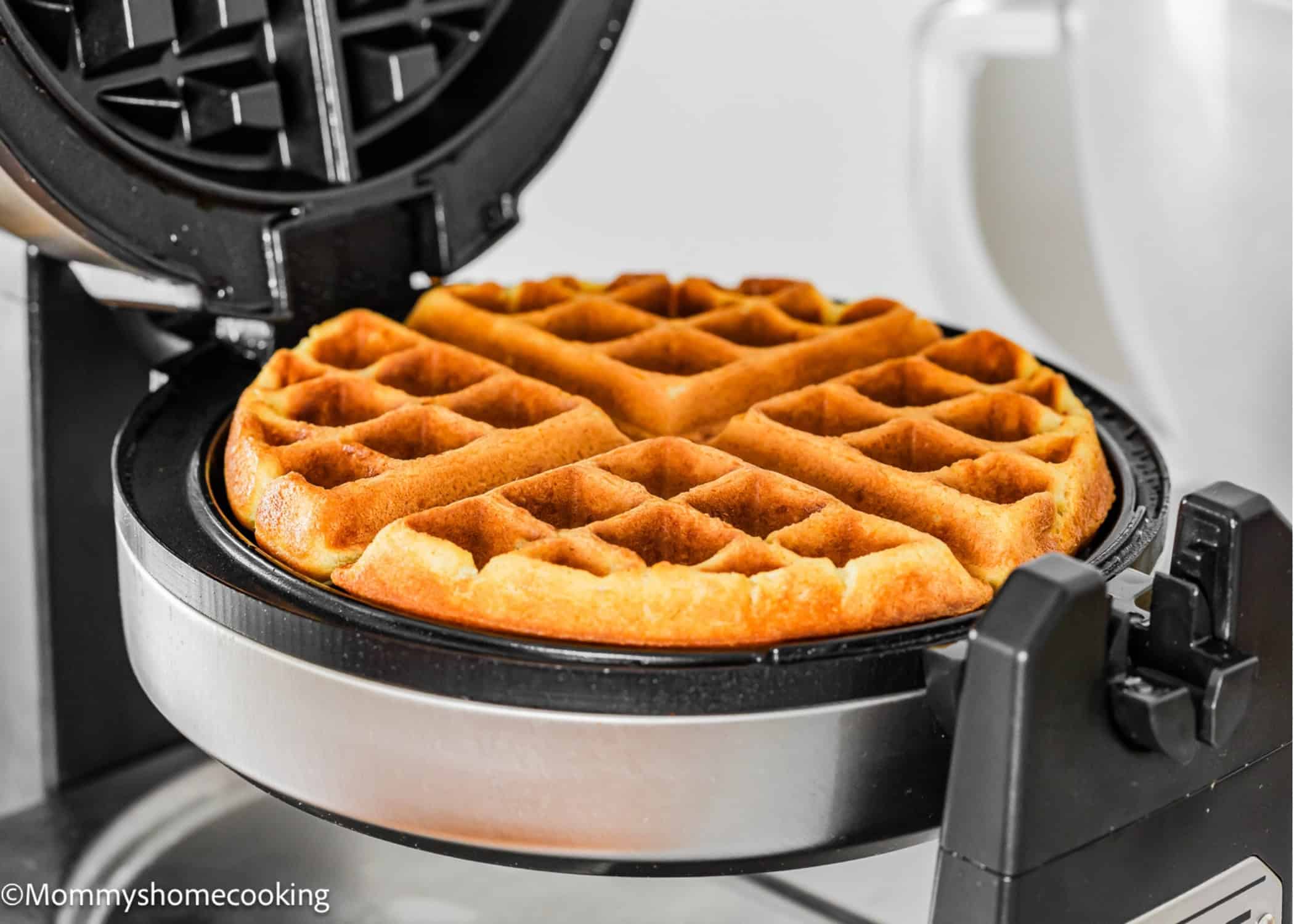 A golden-brown Eggless Yogurt Waffle sits in an open waffle maker, ready to be served.