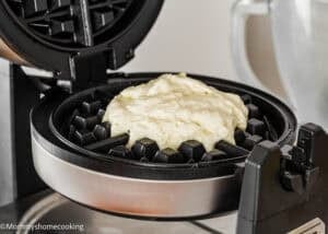 Eggless Yogurt Waffles batter spread on the plates of an open waffle maker, ready to be cooked.