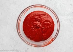 A glass bowl filled with fluffy red velvet waffles (no eggs) batter sits on a light marble surface.