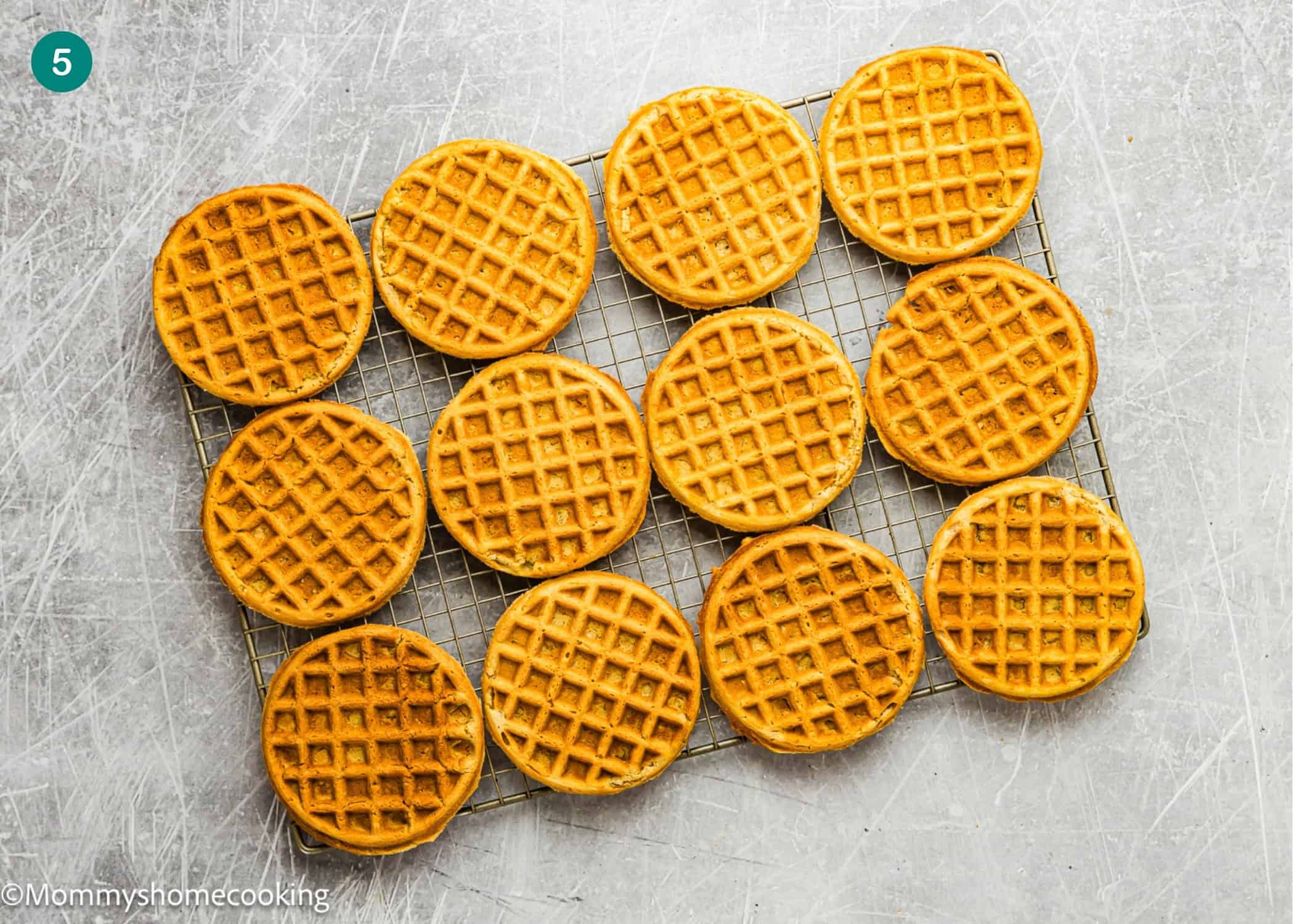 Fourteen egg-free, dairy-free, and refined sugar–free oat waffles are arranged on a cooling rack over a textured gray surface.
