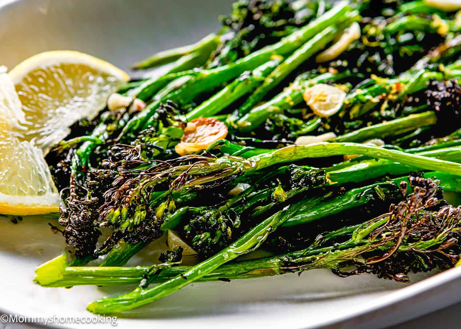 Close-up of Air Fryer Broccolini with Garlic, featuring roasted broccolini and crispy garlic slices, served with lemon wedges on a white plate.