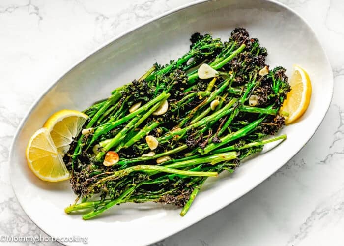 Oval plate with Air Fryer Broccolini with Garlic, sliced garlic, and lemon wedges on a white marble surface.