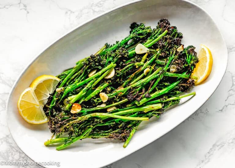 Oval plate with Air Fryer Broccolini with Garlic, sliced garlic, and lemon wedges on a white marble surface.