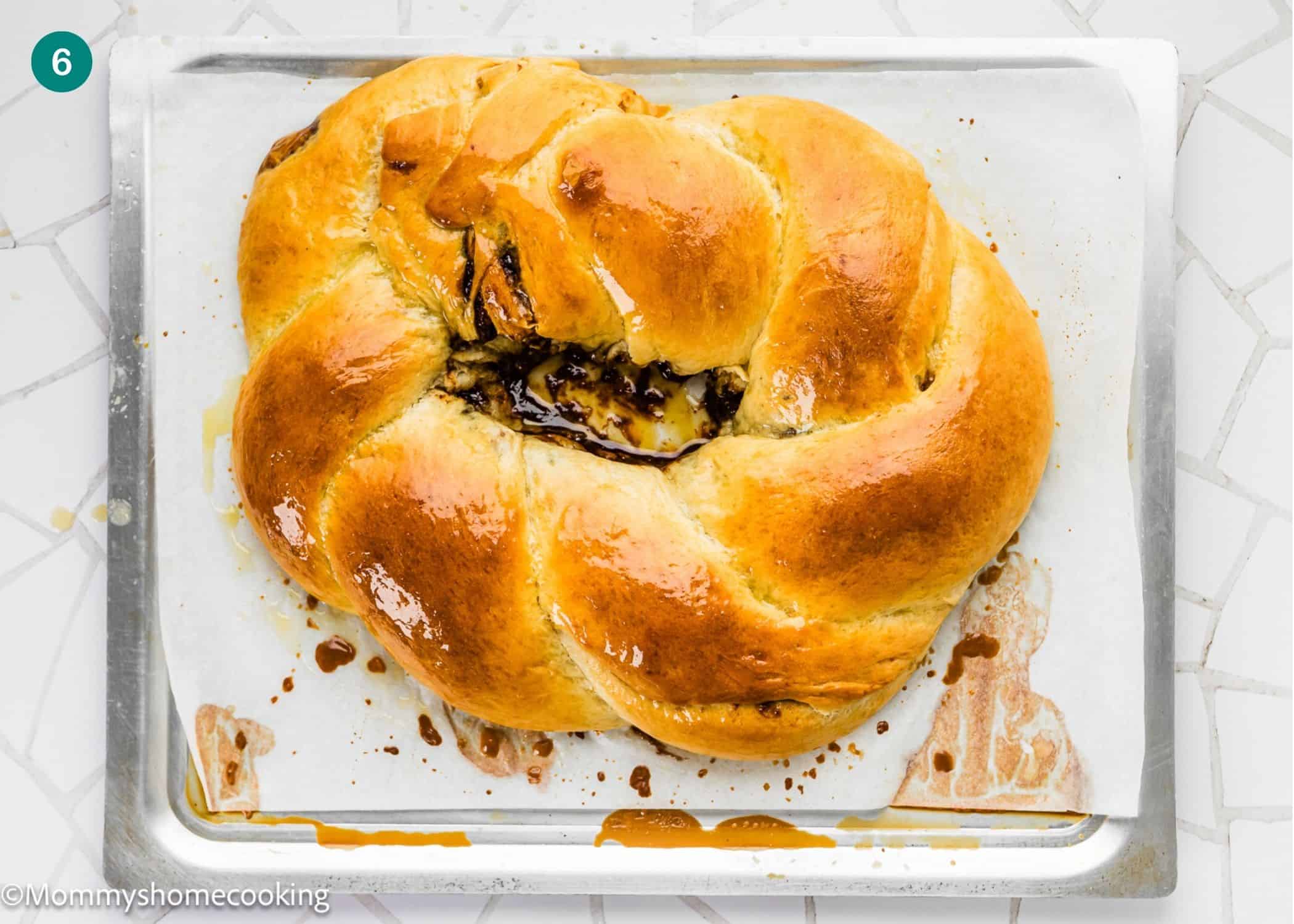 A golden-brown braided bread loaf with a chocolate filling, inspired by the Best Eggless Mardi Gras King Cake, sits on a parchment-lined baking sheet.