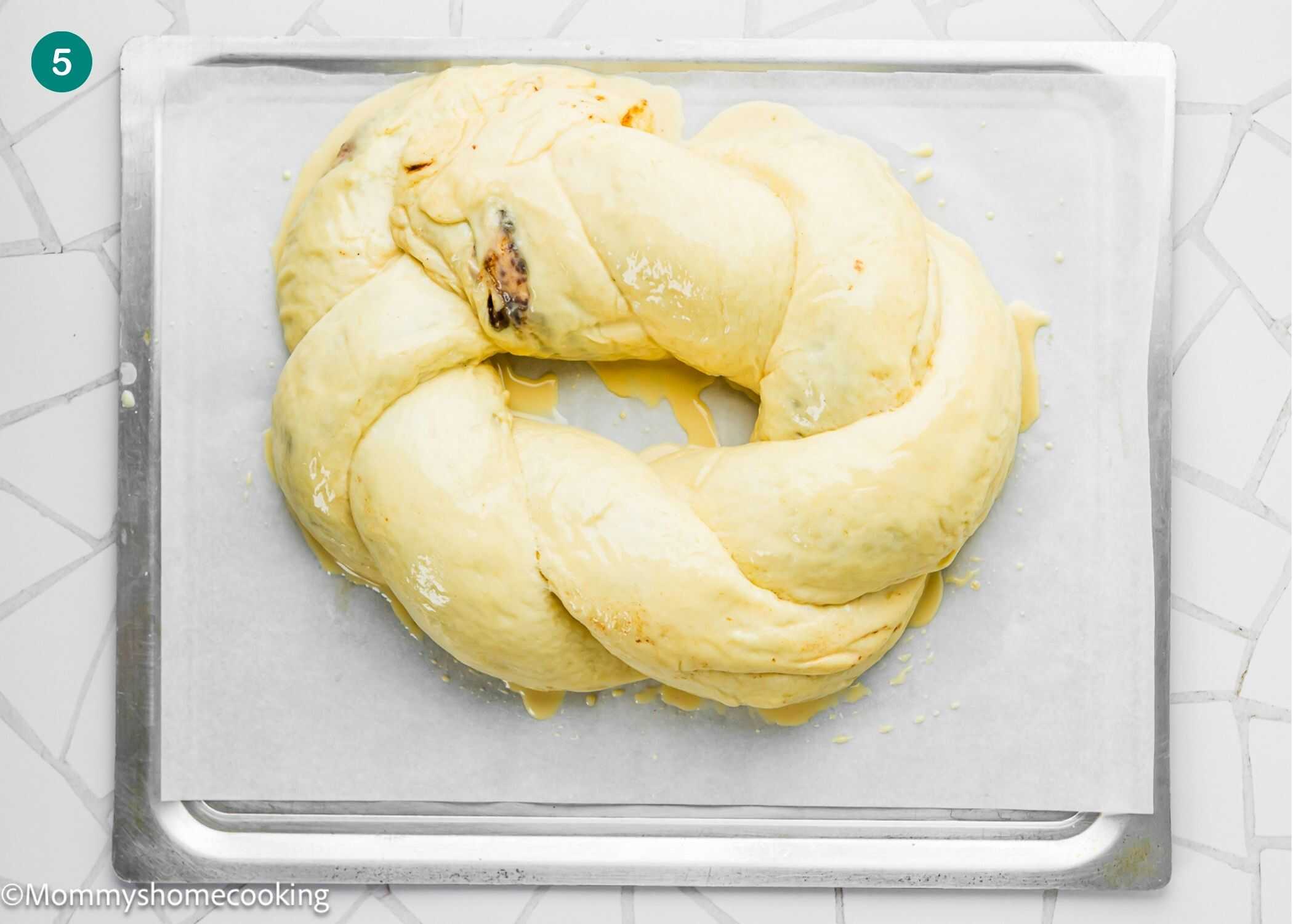 A braided, unbaked dough ring sits on parchment paper atop a baking sheet, ready to become the Best Eggless Mardi Gras King Cake.