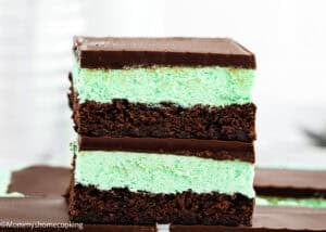 A close-up of two stacked Classic Eggless Mint Chocolate Brownies with a green mint layer between chocolate layers, topped with a smooth chocolate coating.