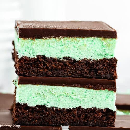 A close-up of two stacked Classic Eggless Mint Chocolate Brownies with a green mint layer between chocolate layers, topped with a smooth chocolate coating.
