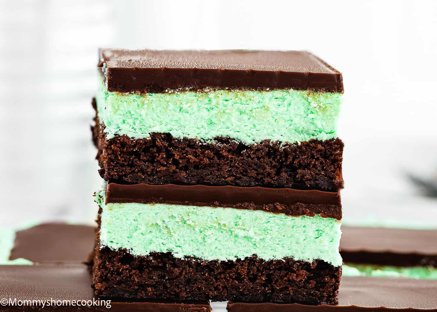 A close-up of two stacked Classic Eggless Mint Chocolate Brownies with a green mint layer between chocolate layers, topped with a smooth chocolate coating.