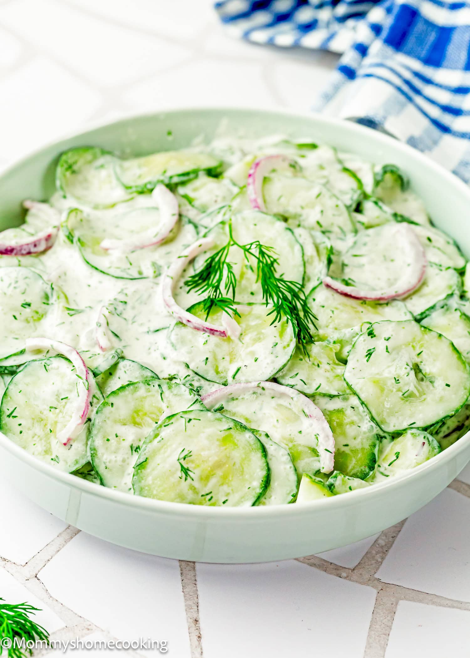 A bowl of Creamy Cucumber Salad (Egg-Free) features sliced cucumbers, red onions, fresh dill, and a light dressing, garnished with a dill sprig.