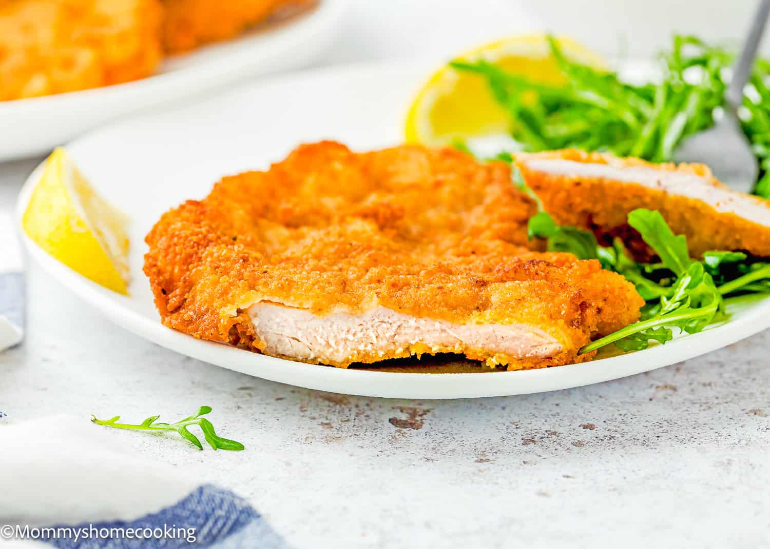 Crispy Eggless Pork Schnitzel (egg and dairy free) served on a white plate with fresh arugula and a lemon wedge.