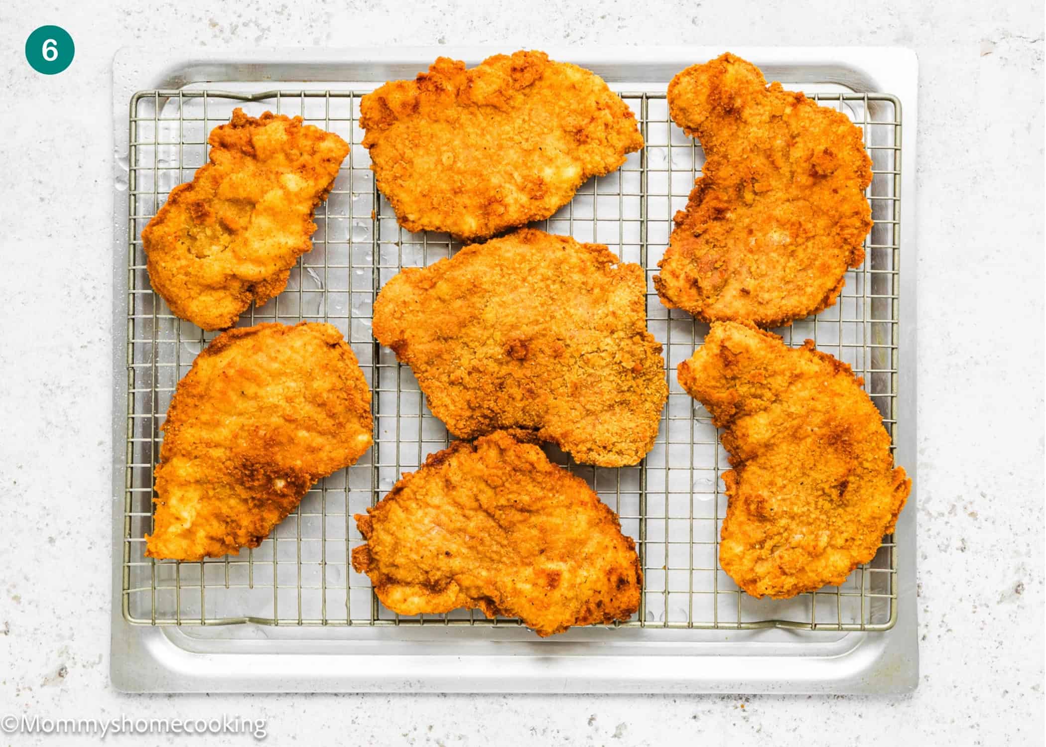 Seven pieces of golden-brown Crispy Eggless Pork Schnitzel (egg and dairy free) cool on a wire rack placed over a baking sheet.