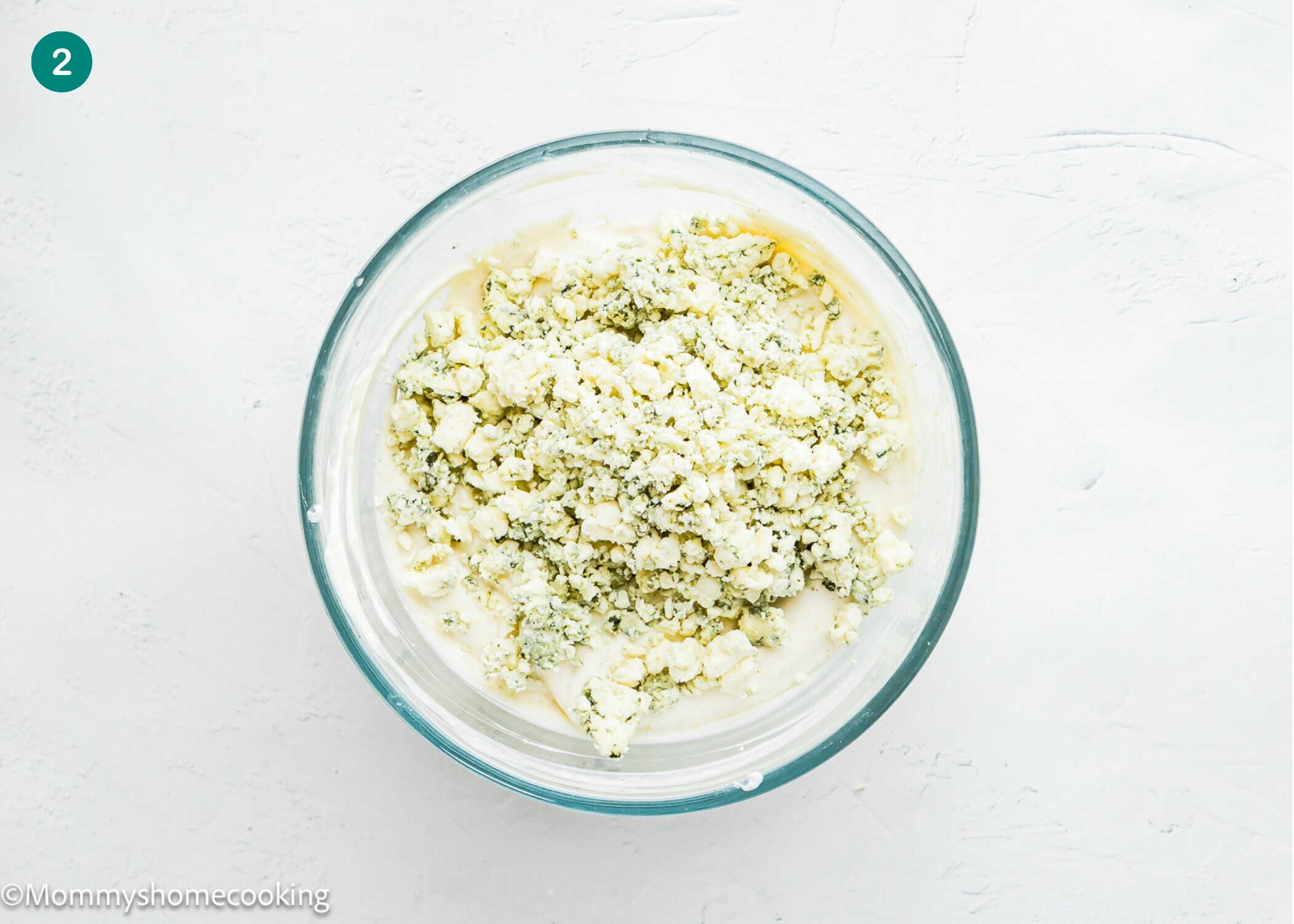 A glass bowl filled with a mixture of crumbled ricotta and spinach sits on a white surface, perfect for pairing with Easy Eggless Blue Cheese Dressing.