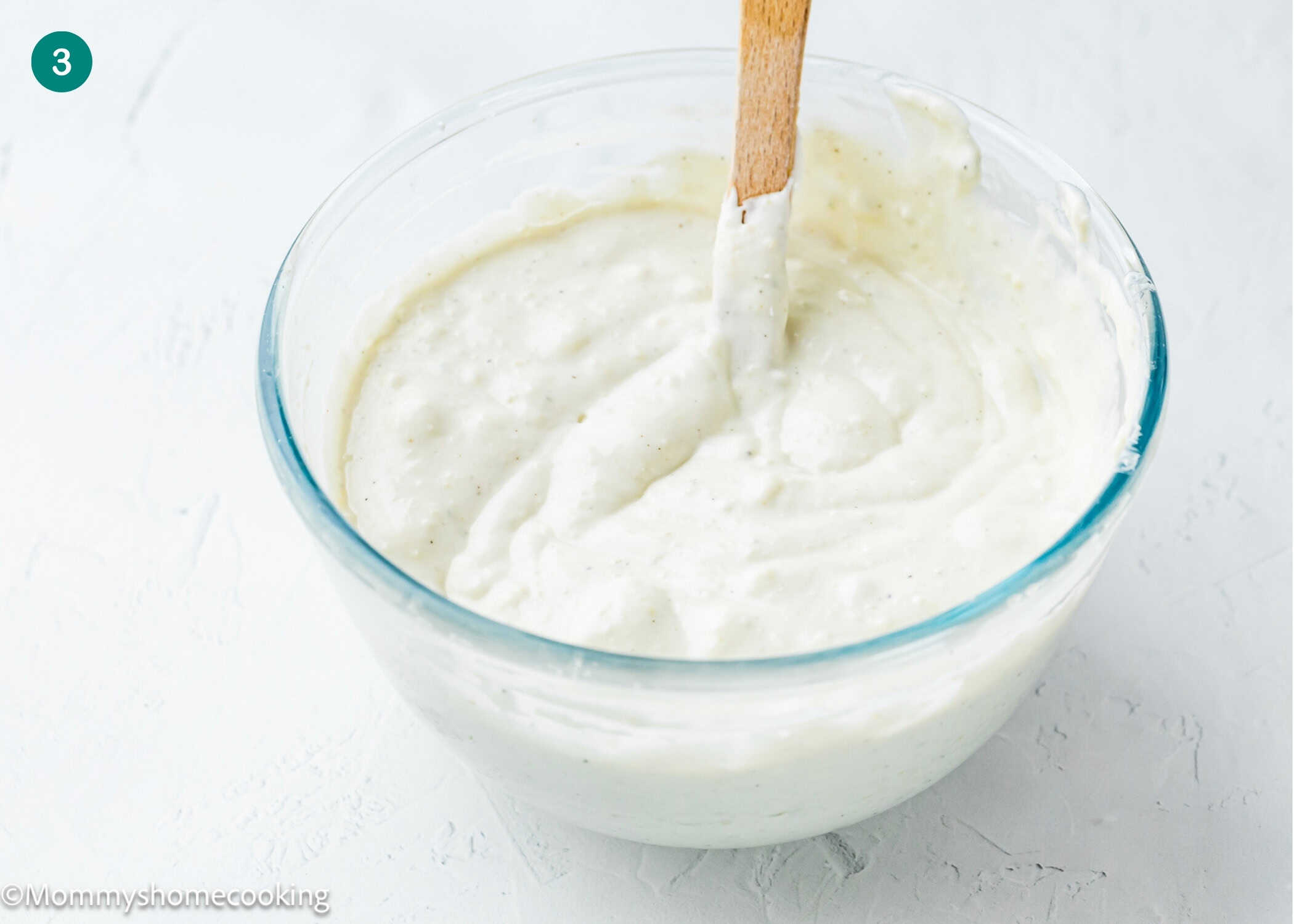 A glass bowl filled with thick, creamy Easy Eggless Blue Cheese Dressing is shown, with a wooden spatula resting inside.