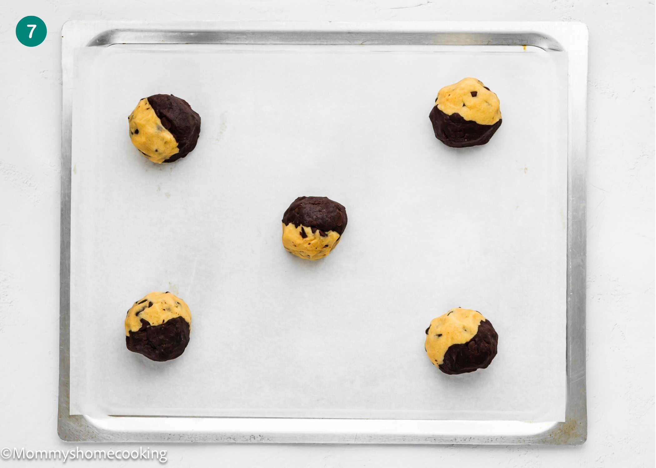 Five balls of eggless Brookie Cookies (one dough), yellow and dark brown, are spaced apart on a parchment-lined baking sheet.