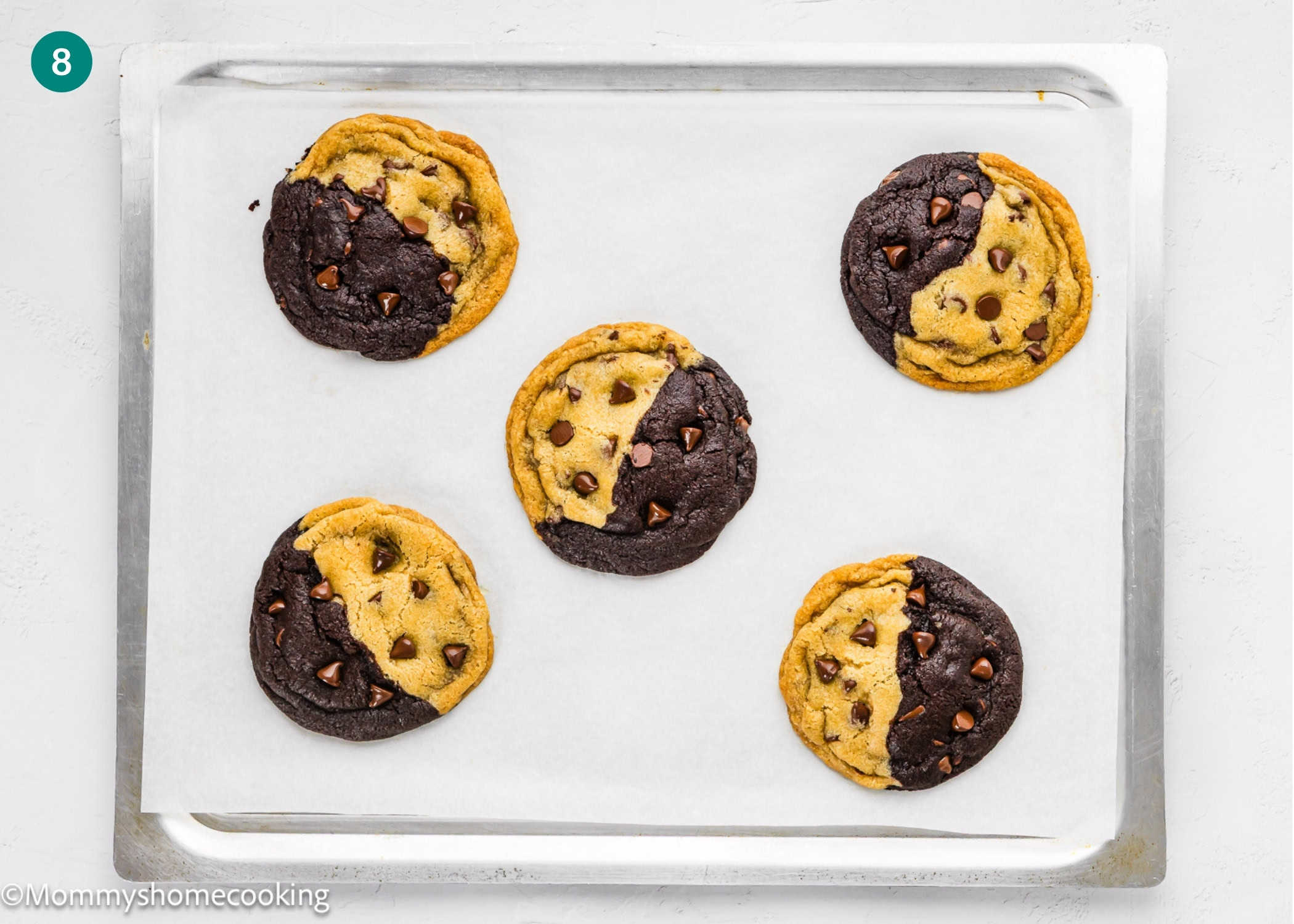 A baking sheet with five Eggless Brookie Cookies (One Dough), each half-chocolate, half-vanilla chip, on parchment paper.