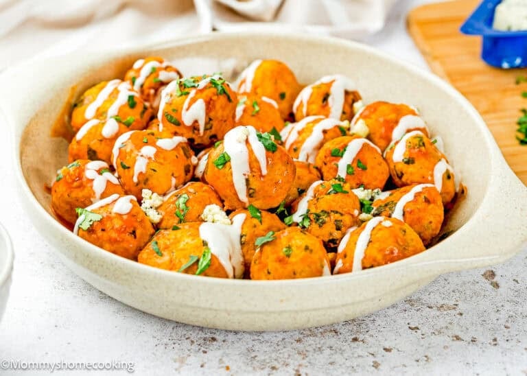 A bowl of Eggless Buffalo Chicken Meatballs garnished with chopped herbs, drizzled with ranch dressing, and sprinkled with blue cheese.