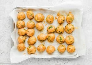A baking sheet lined with parchment paper holds 24 evenly spaced Eggless Buffalo Chicken Meatballs, garnished with chopped herbs.