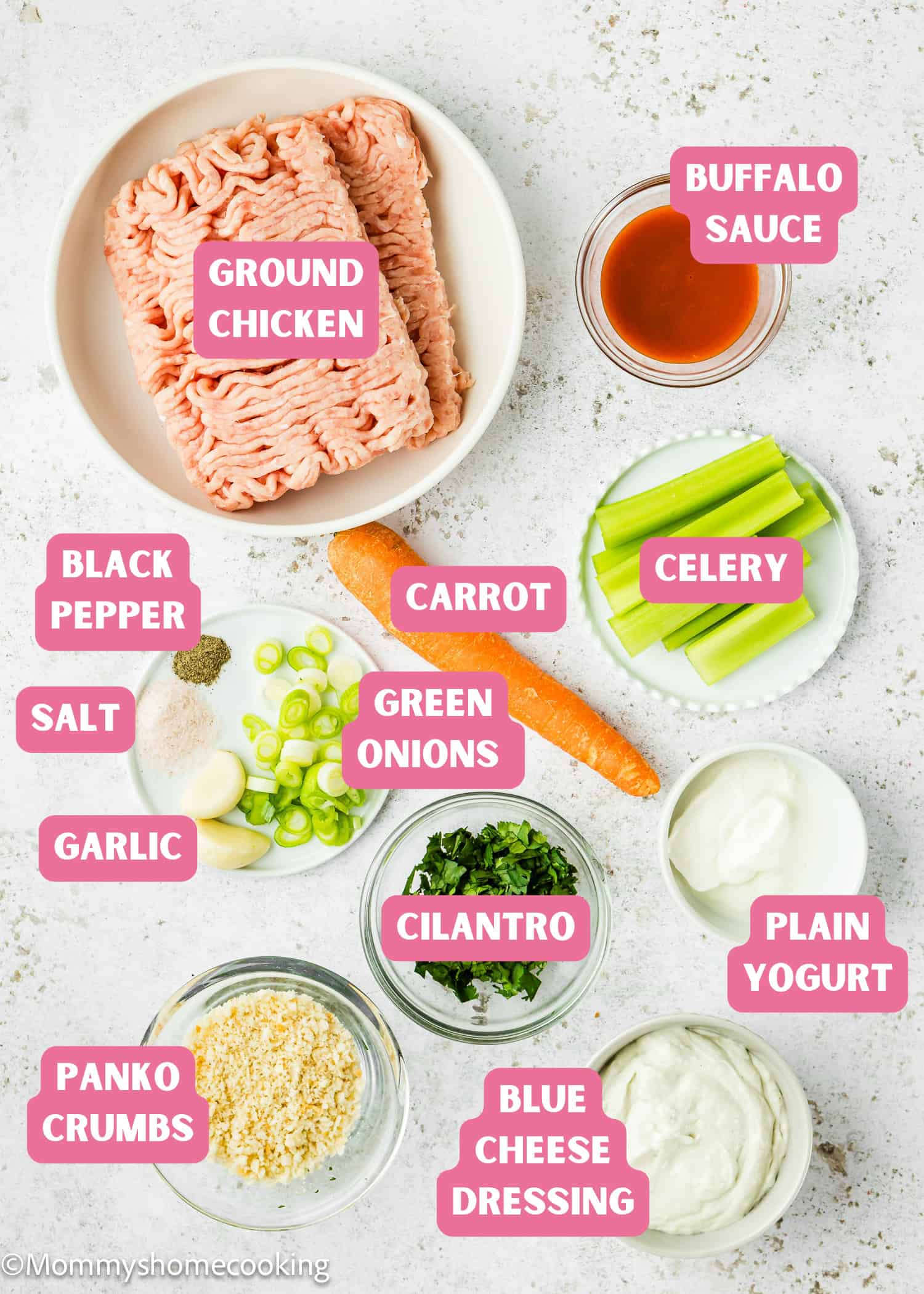 Ingredients for Eggless Buffalo Chicken Meatballs arranged on a white surface, including ground chicken, panko crumbs, garlic, spices, herbs, buffalo sauce, celery, carrot, yogurt, and blue cheese dressing.
