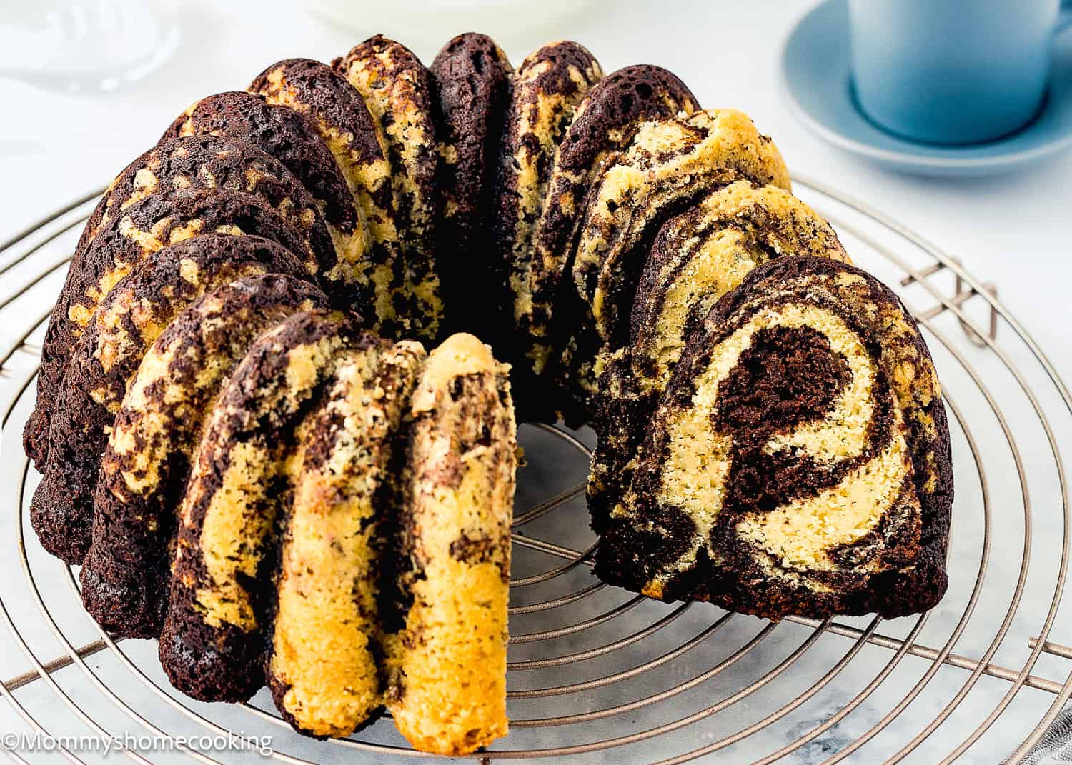 An Eggless Marble Bundt Cake with visible swirls of chocolate and vanilla, sliced and arranged on a round cooling rack.