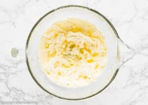 A glass mixing bowl with creamed butter and sugar mixture sits on a white marble surface, ready to become a delicious Eggless Marble Bundt Cake.