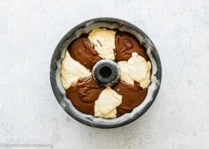 An Eggless Marble Bundt Cake pan filled with alternating sections of chocolate and vanilla cake batter, ready to be baked.