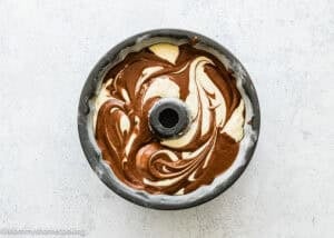 An Eggless Marble Bundt Cake pan filled with swirled chocolate and vanilla cake batter, ready to be baked, seen from above.