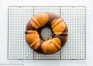 An Eggless Marble Bundt Cake cooling on a wire rack over a white textured surface.