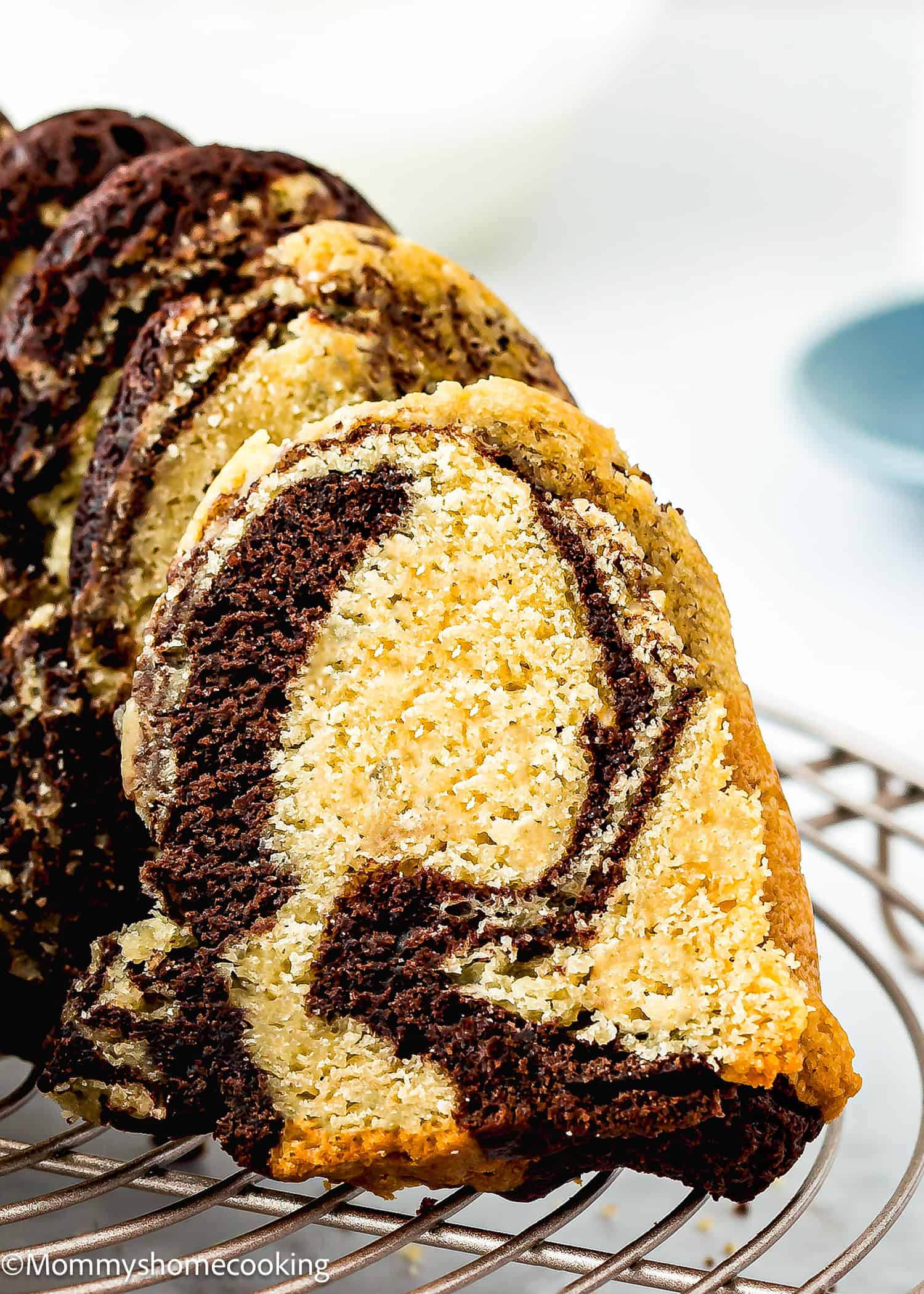 A close-up of an Eggless Marble Bundt Cake, sliced to reveal chocolate and vanilla swirls, placed on a cooling rack.