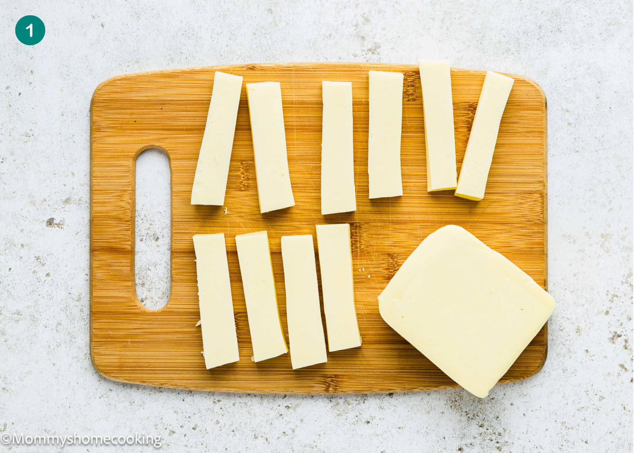 Rectangular slices of white cheese, perfect for making Eggless Mozzarella Sticks, are arranged on a wooden cutting board with a solid block of cheese beside them.