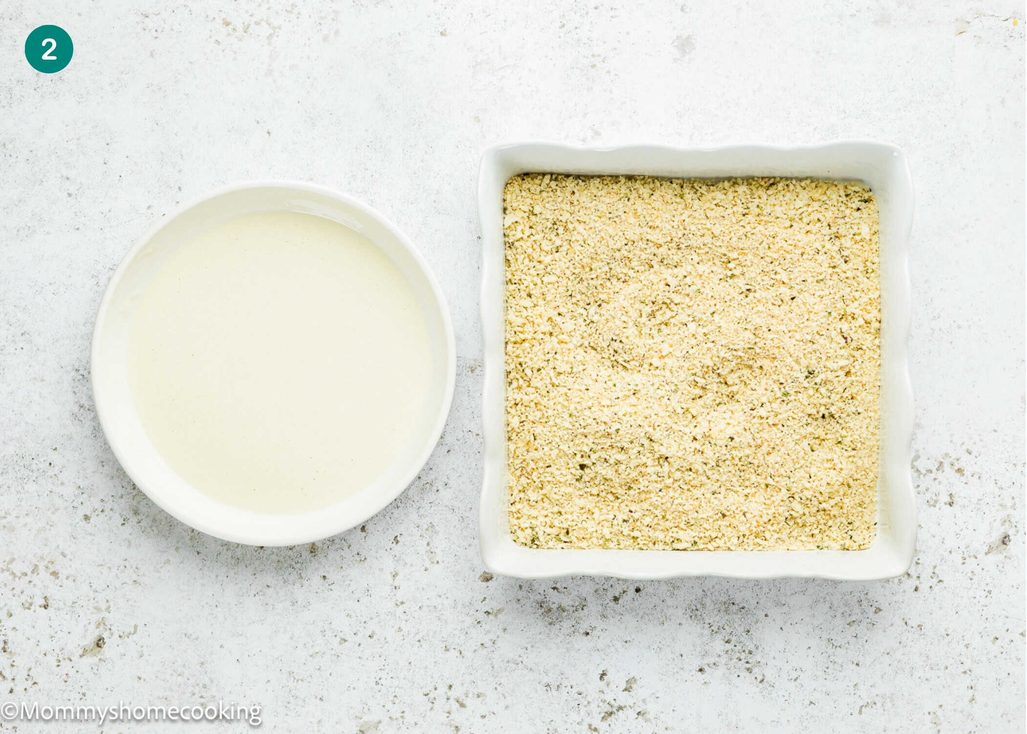 A round bowl of liquid batter sits next to a square dish filled with breadcrumbs on a light, textured surface, ready for making Eggless Mozzarella Sticks.