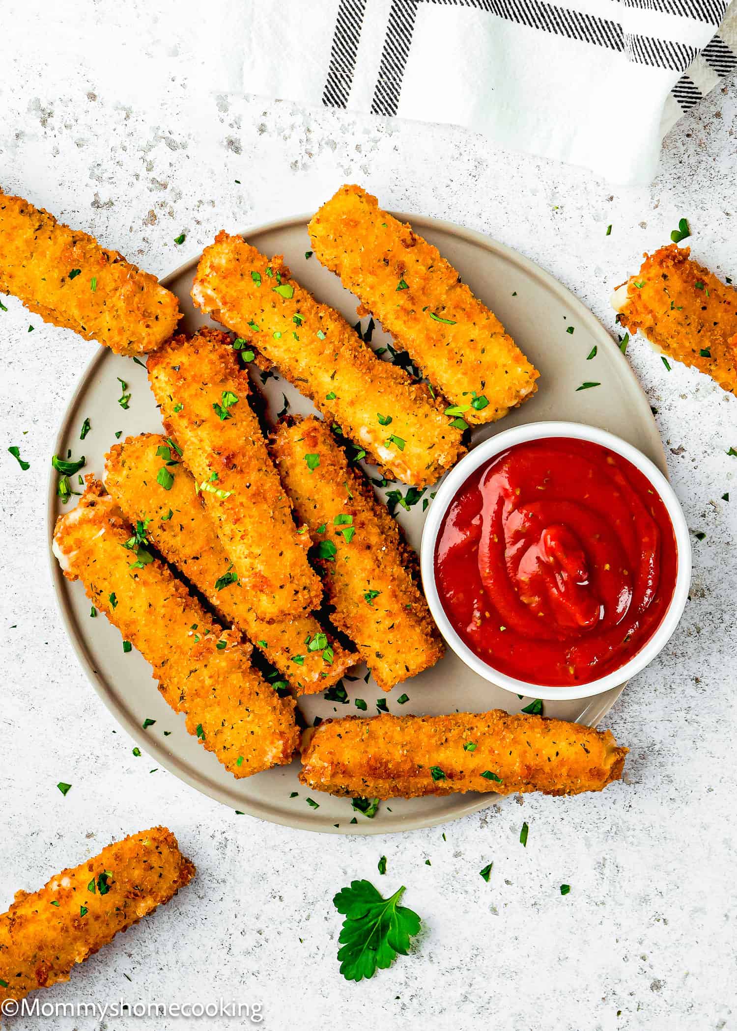A plate of Eggless Mozzarella Sticks is arranged around a small bowl of marinara sauce, with a white cloth napkin in the background.