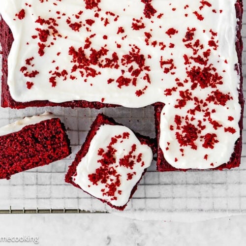 Eggless Red Velvet Sheet Cake with white icing and red cake crumbs on top, placed on a wire rack, with two slices cut and separated from the main cake.