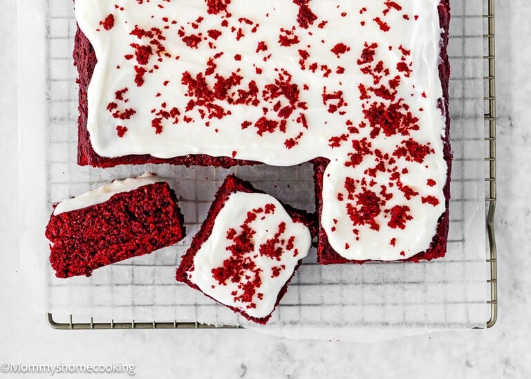 Eggless Red Velvet Sheet Cake with white icing and red cake crumbs on top, placed on a wire rack, with two slices cut and separated from the main cake.
