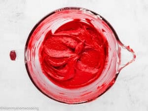 A glass mixing bowl filled with smooth Eggless Red Velvet Sheet Cake batter sits on a white surface.