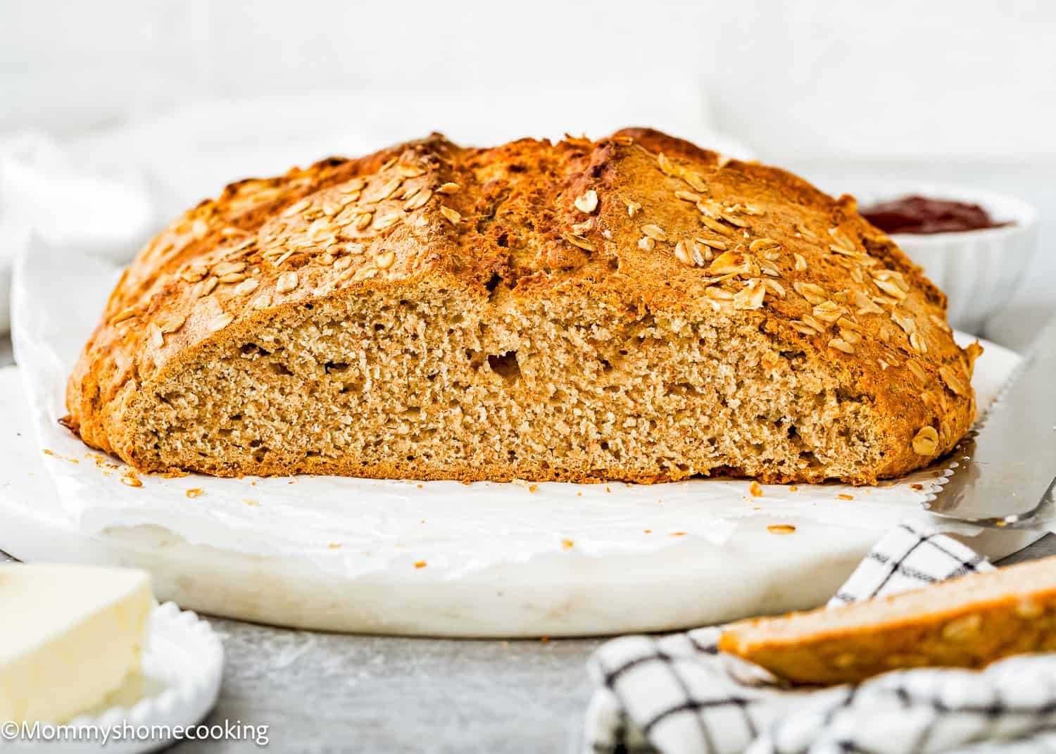 A loaf of Irish Soda Bread (No eggs!), sliced in half to show the texture inside, sits on parchment paper with butter and jam in the background.