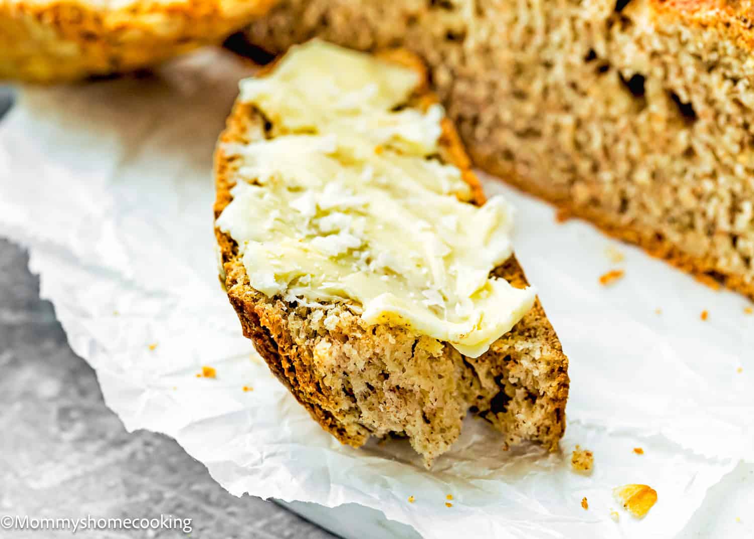 A slice of Irish Soda Bread (No eggs!) with butter spread on top, placed on a sheet of white parchment paper.