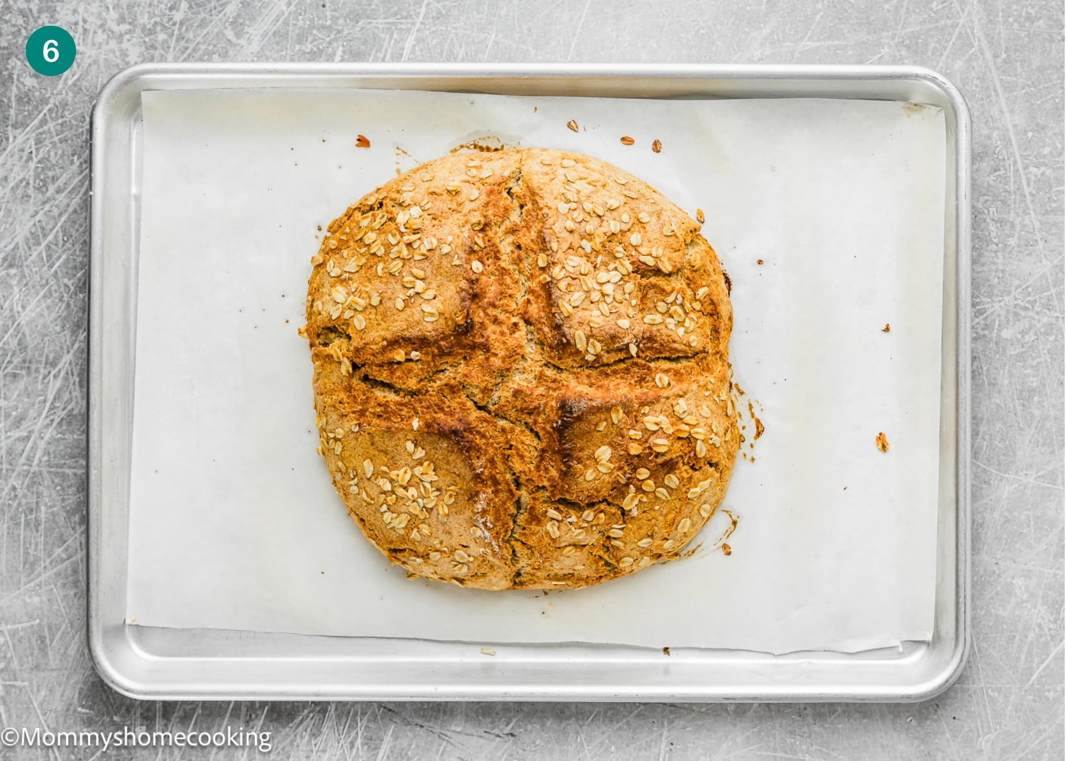 A round loaf of Irish Soda Bread (No eggs!) with an oat topping and a cross cut on top sits on parchment paper on a baking sheet.