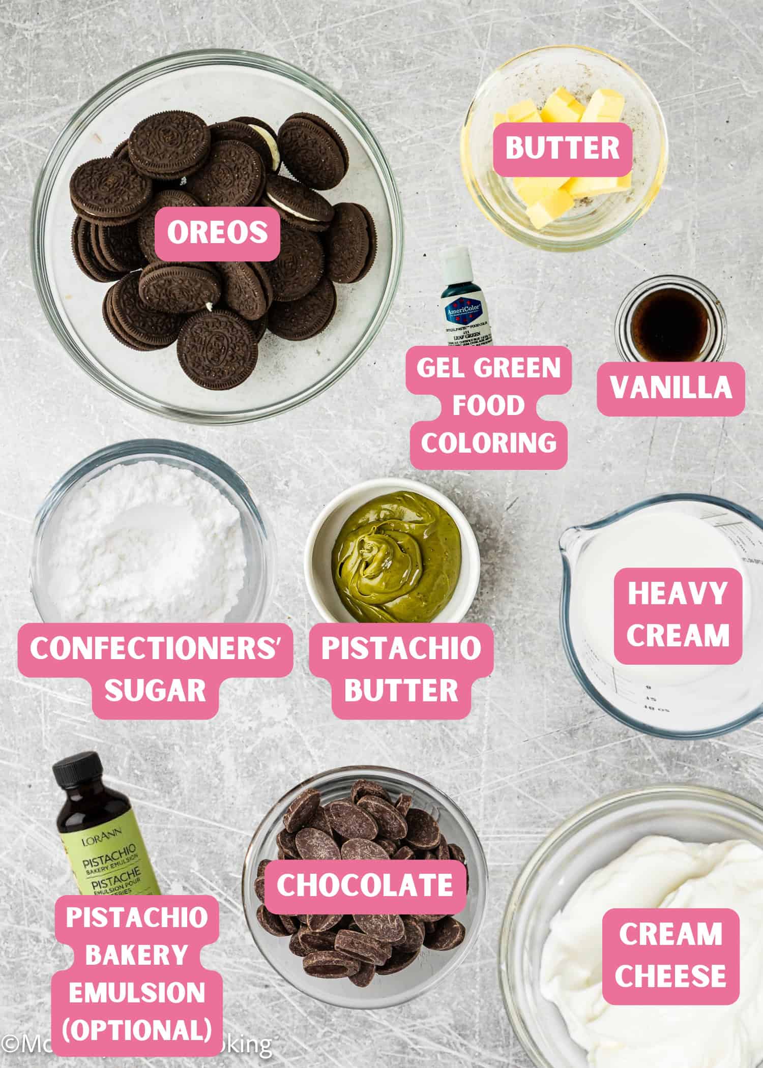 Various labeled ingredients for No Bake Pistachio Chocolate Cheesecake Pie, including Oreo cookies, butter, gel green food coloring, vanilla, heavy cream, cream cheese, chocolate, pistachio cream, confectioners' sugar, and pistachio emulsion.