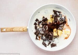 A white pan with chopped dark chocolate, cubes of butter, cocoa powder, and cream before mixing for an Ultra-Fudgy Eggless Chocolate Layer Cake (Matilda Inspired).