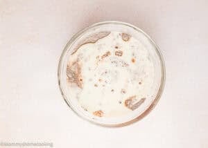 A glass bowl containing cocoa powder, sugar, and milk mixture seen from above on a light-colored surface—the first step for an Ultra-Fudgy Eggless Chocolate Layer Cake (Matilda Inspired).