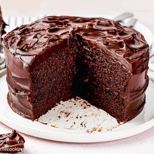 An ultra-fudgy eggless chocolate layer cake (Matilda inspired) with rich chocolate frosting, sliced to show the moist inside, sits on a white plate.